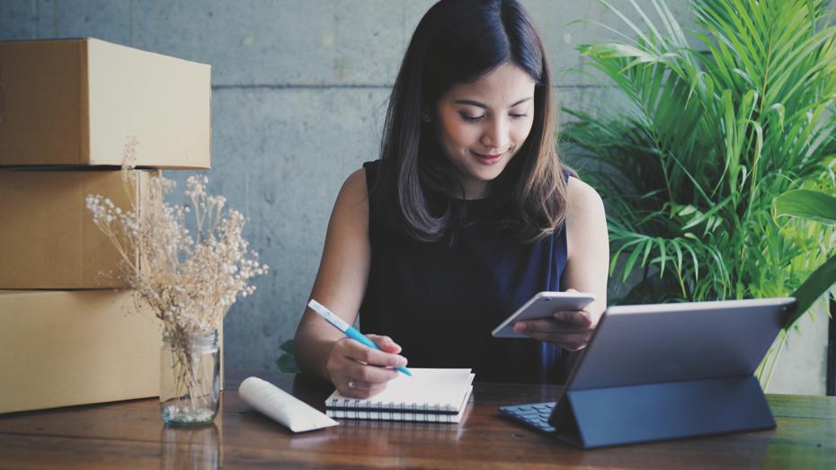 woman sat writing on notepad while on phone